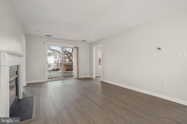 unfurnished living room with visible vents, baseboards, dark wood finished floors, a glass covered fireplace, and a textured ceiling