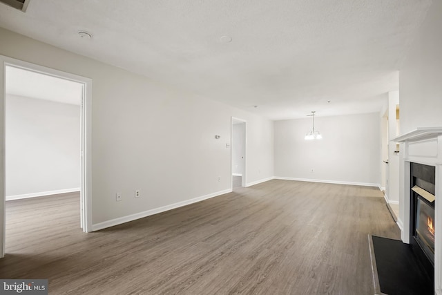 unfurnished living room featuring an inviting chandelier, baseboards, wood finished floors, and a glass covered fireplace