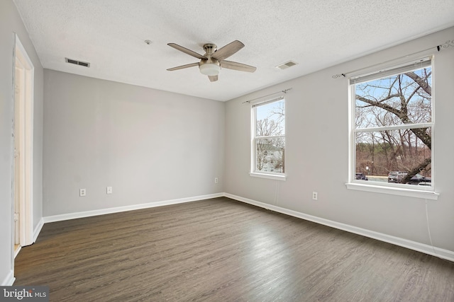 spare room with baseboards, visible vents, a ceiling fan, dark wood-style flooring, and a textured ceiling