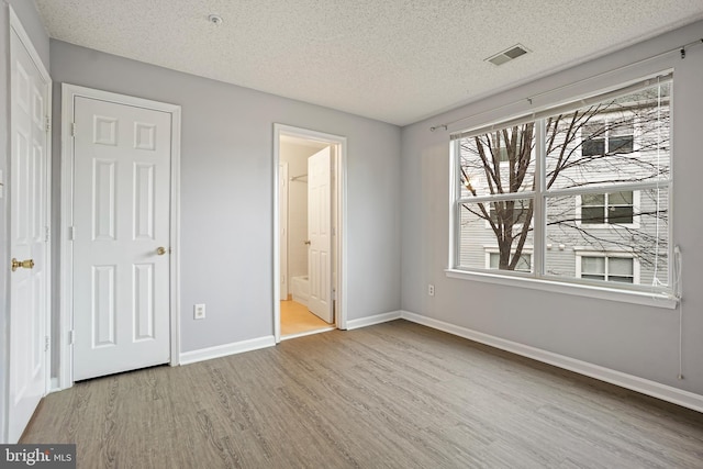 unfurnished bedroom with baseboards, visible vents, ensuite bath, wood finished floors, and a textured ceiling