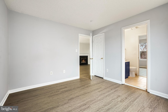 unfurnished bedroom featuring a warm lit fireplace, baseboards, visible vents, and wood finished floors