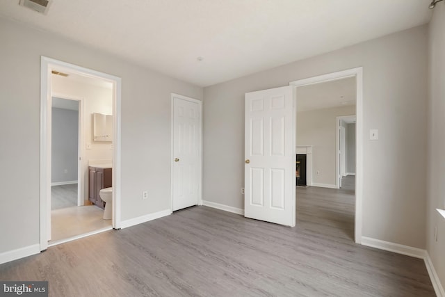 unfurnished bedroom with connected bathroom, wood finished floors, visible vents, baseboards, and a lit fireplace