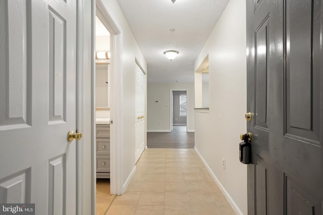 hall featuring light tile patterned floors, a textured ceiling, and baseboards