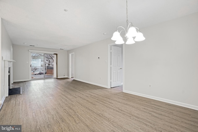 unfurnished living room with a chandelier, a fireplace, wood finished floors, and baseboards