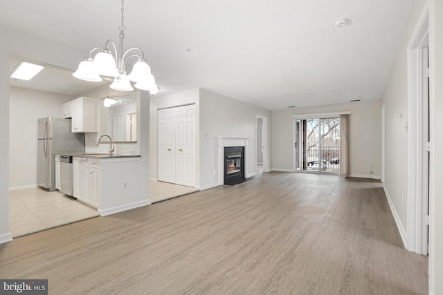 unfurnished living room with light wood-style flooring, baseboards, a sink, and a fireplace with flush hearth