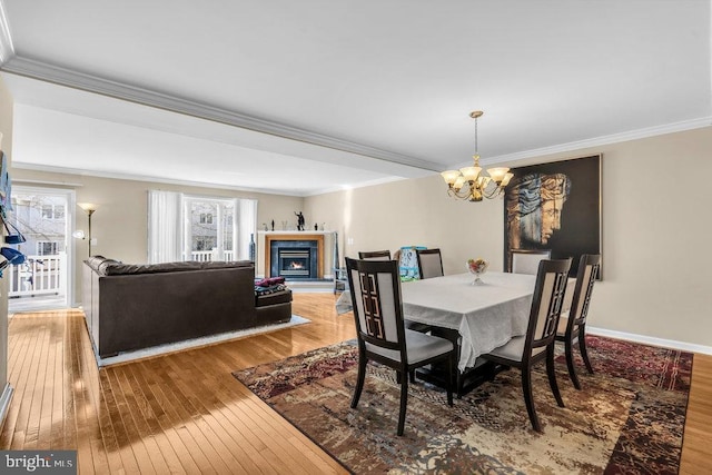 dining area featuring baseboards, crown molding, a lit fireplace, and hardwood / wood-style floors