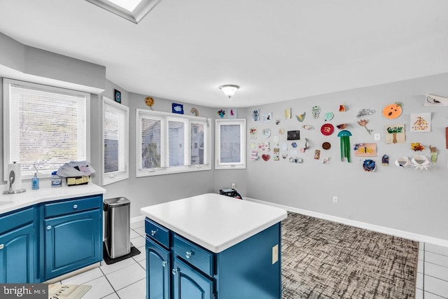 kitchen with baseboards, light tile patterned flooring, light countertops, blue cabinets, and a center island