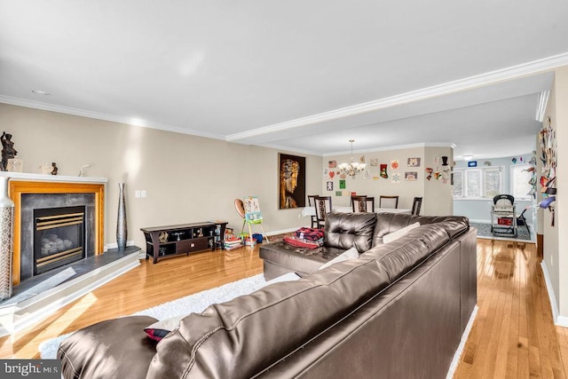 living room featuring baseboards, an inviting chandelier, ornamental molding, a glass covered fireplace, and light wood-type flooring