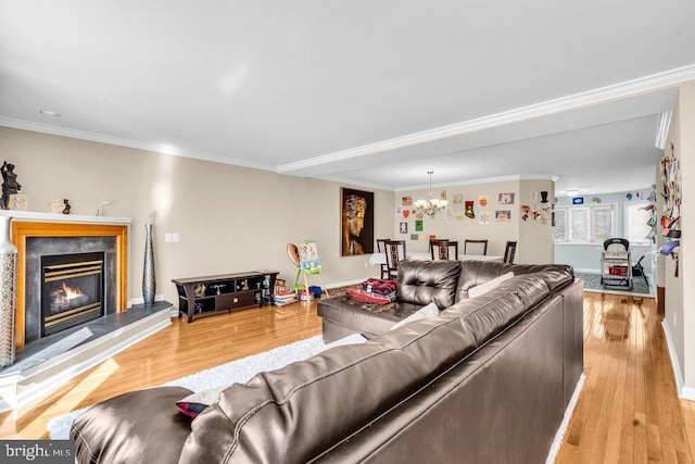 living area featuring baseboards, light wood-type flooring, a glass covered fireplace, ornamental molding, and a notable chandelier