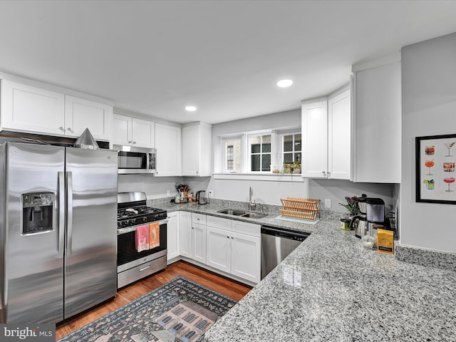 kitchen featuring light stone counters, wood finished floors, a sink, white cabinets, and appliances with stainless steel finishes