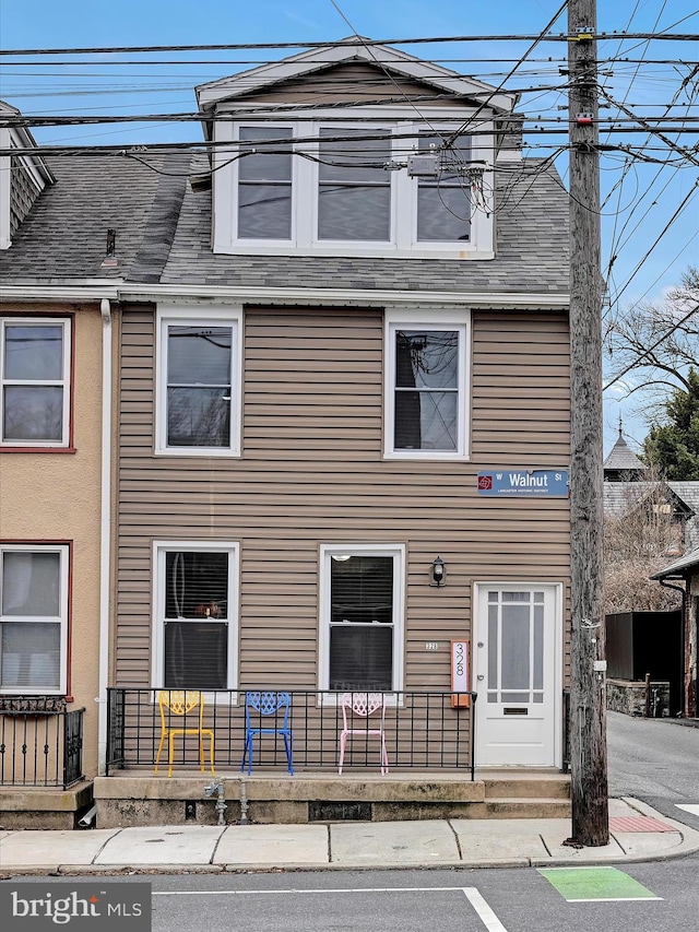 view of front of house featuring a porch, roof with shingles, and a chimney