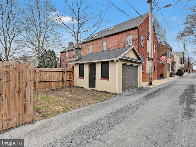 view of property exterior featuring stucco siding, fence, roof with shingles, a garage, and brick siding