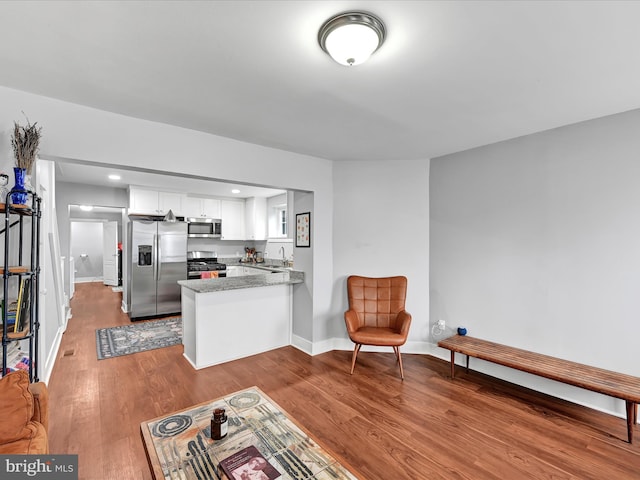 interior space with a sink, wood finished floors, stainless steel appliances, a peninsula, and white cabinets