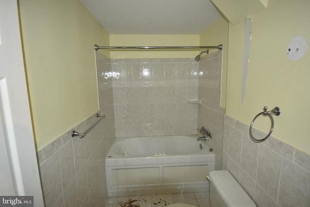 bathroom featuring toilet, wainscoting, tub / shower combination, and tile walls