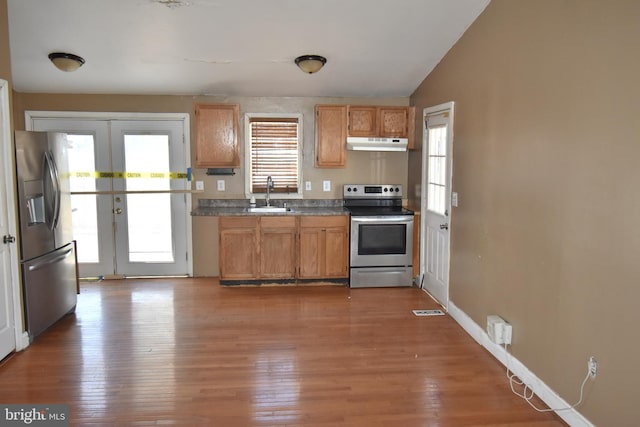 kitchen featuring light wood-style floors, stainless steel appliances, french doors, under cabinet range hood, and a sink