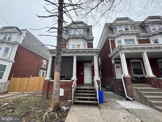 view of front facade featuring covered porch, brick siding, fence, and mansard roof