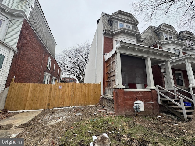 view of side of home featuring a porch, brick siding, fence, and mansard roof