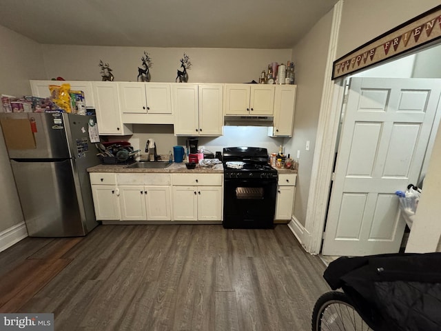 kitchen with dark wood-style floors, freestanding refrigerator, black gas stove, a sink, and under cabinet range hood