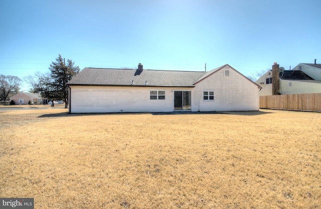 rear view of property with a shingled roof, a yard, and fence