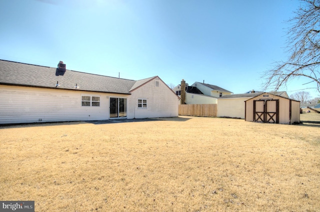 rear view of property with fence, roof with shingles, a chimney, an outbuilding, and a storage unit