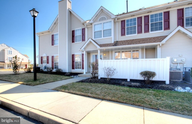 view of property with central air condition unit, covered porch, a front yard, a shingled roof, and a chimney