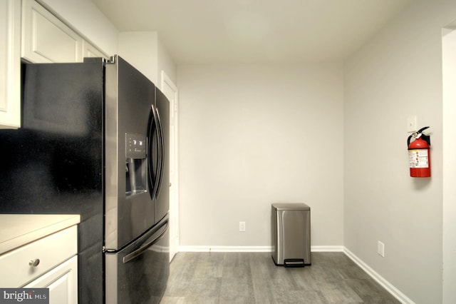 kitchen with baseboards, light countertops, white cabinets, light wood-style floors, and black fridge