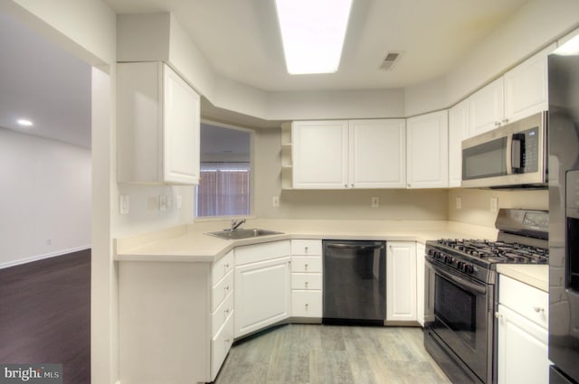 kitchen with light wood finished floors, appliances with stainless steel finishes, white cabinetry, and a sink