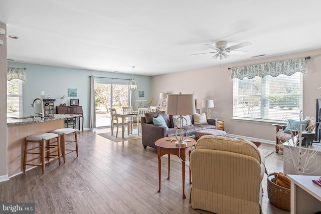 living area with visible vents, ceiling fan, baseboards, and wood finished floors