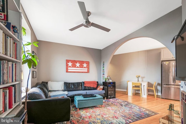 living room featuring light wood finished floors, ceiling fan, arched walkways, and baseboards