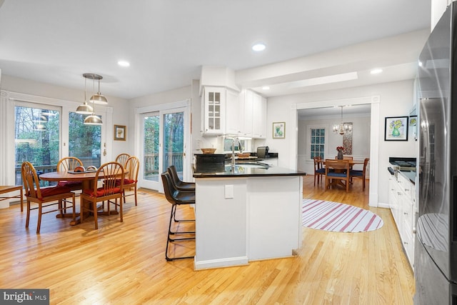 kitchen with light wood finished floors, dark countertops, freestanding refrigerator, white cabinets, and a sink