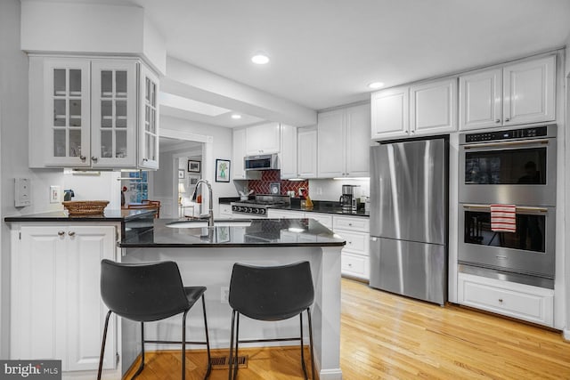 kitchen with a breakfast bar, stainless steel appliances, glass insert cabinets, a sink, and a peninsula