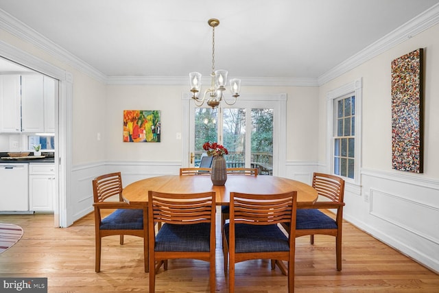 dining area with ornamental molding, wainscoting, light wood-style flooring, and an inviting chandelier