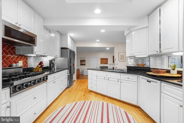 kitchen with light wood finished floors, appliances with stainless steel finishes, a peninsula, white cabinetry, and a sink