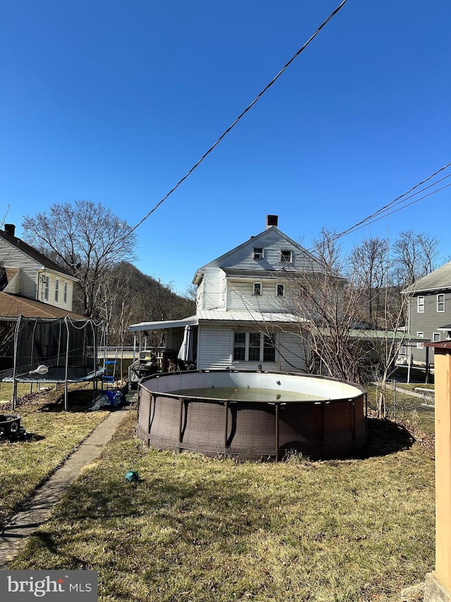 back of house with a trampoline and an outdoor pool