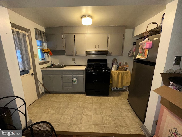 kitchen with black gas range, under cabinet range hood, a sink, gray cabinets, and freestanding refrigerator