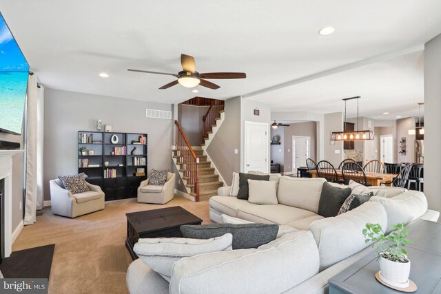 living room with recessed lighting, light colored carpet, a fireplace with flush hearth, visible vents, and stairs