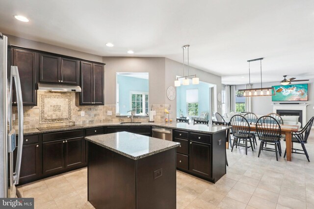 kitchen featuring under cabinet range hood, stainless steel appliances, a fireplace, a kitchen island, and light stone countertops