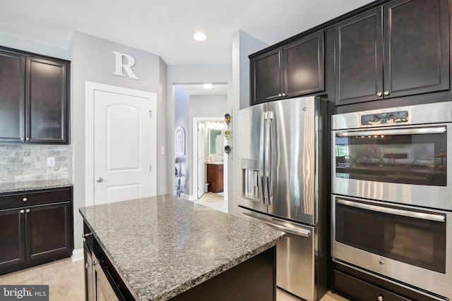 kitchen with stone counters, light tile patterned floors, stainless steel appliances, tasteful backsplash, and dark brown cabinets