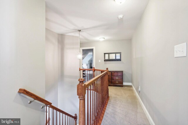 hall featuring baseboards, light carpet, and an upstairs landing