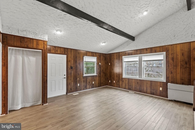 empty room with lofted ceiling with beams, wood walls, a textured ceiling, and wood finished floors