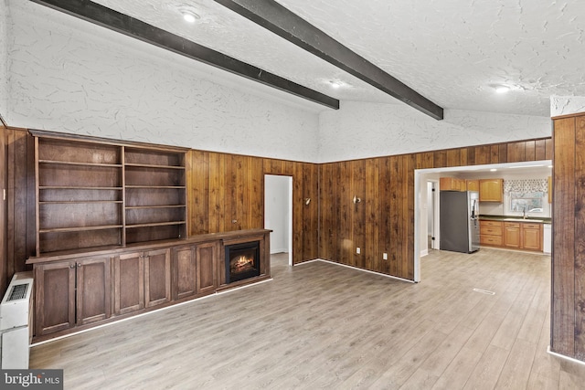 unfurnished living room featuring lofted ceiling with beams, wood walls, a textured ceiling, light wood-type flooring, and a warm lit fireplace