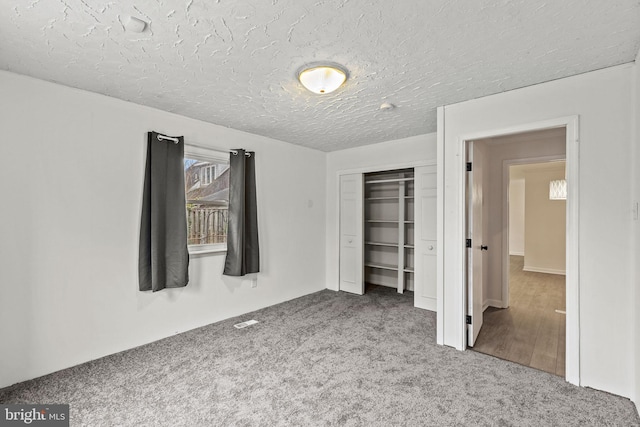 unfurnished bedroom featuring carpet, a textured ceiling, visible vents, and a closet