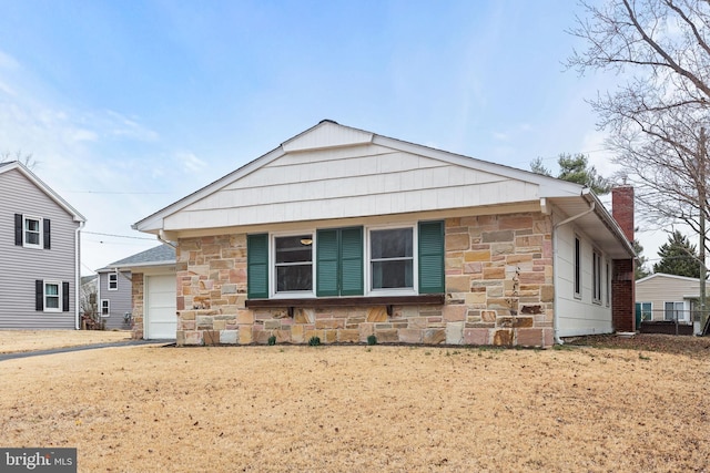 view of front of home with driveway, stone siding, and a chimney