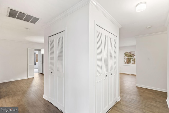 hallway featuring baseboards, visible vents, wood finished floors, and ornamental molding