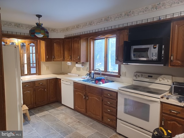 kitchen featuring light countertops, white appliances, a sink, and brown cabinets