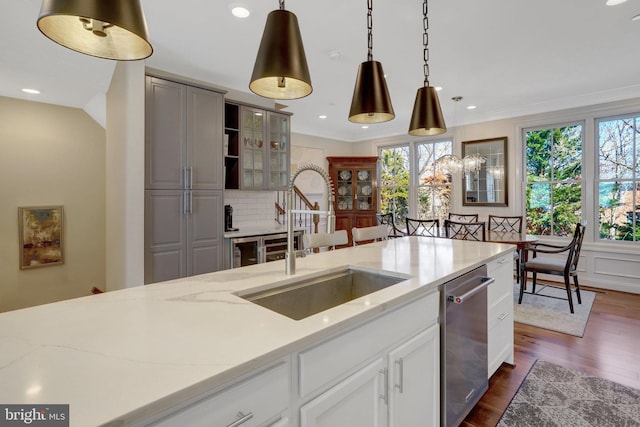 kitchen with a sink, light stone counters, stainless steel dishwasher, dark wood finished floors, and hanging light fixtures