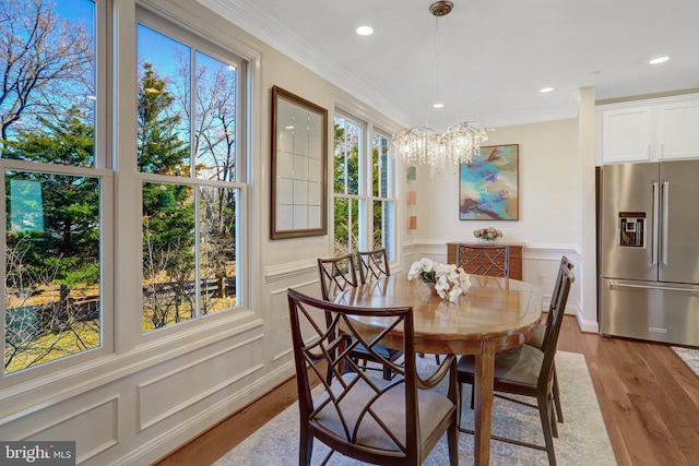 dining room with light wood finished floors, ornamental molding, and a decorative wall