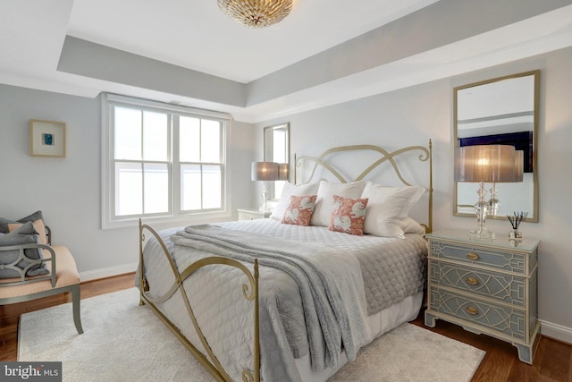 bedroom with a raised ceiling, baseboards, and wood finished floors