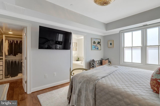 bedroom featuring wood finished floors, visible vents, baseboards, ensuite bath, and a spacious closet