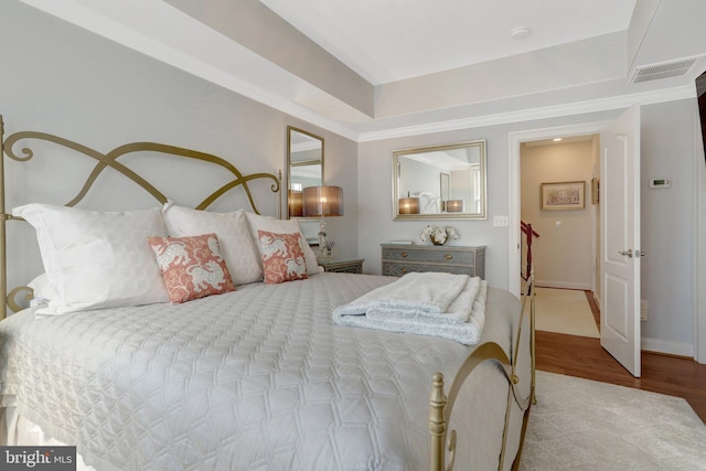 bedroom with visible vents, baseboards, wood finished floors, and ornamental molding